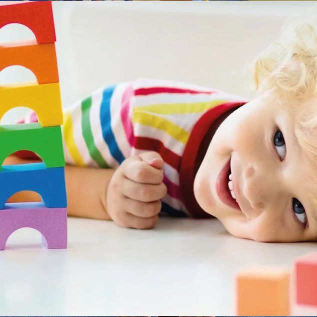 Bimbo sorridente sdraiato accanto a una torre di costruzioni arcobaleno