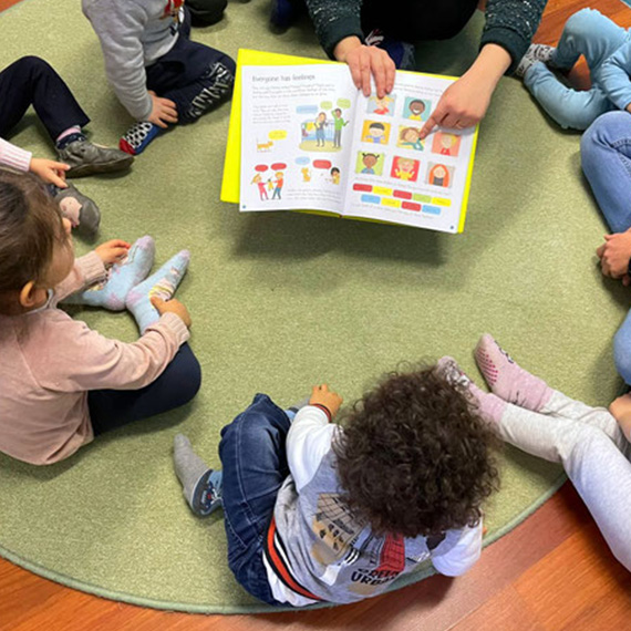 Gruppo di bambini in cerchio mentre l'educatrice legge un libro in inglese