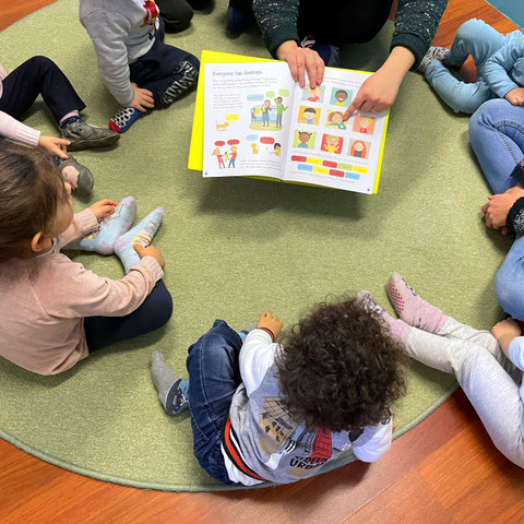 Bambini seduti in cerchio mentre l’educatrice legge un libro illustrato
